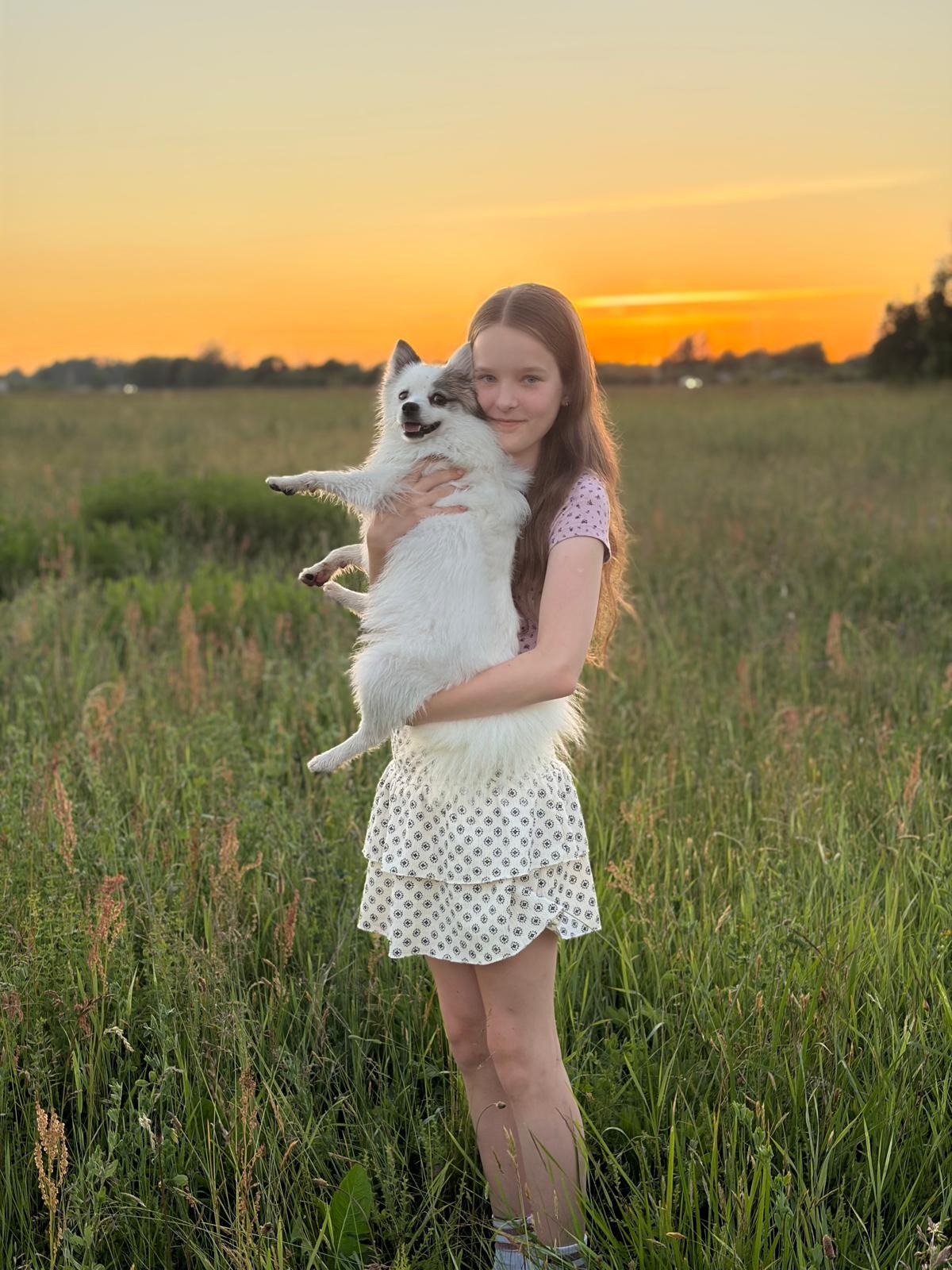 Annija ar savu sunīti saulrieta pielietā pļavā
